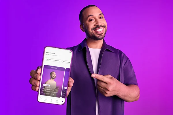 Pessoa aponta para celular exibindo tela do app Vivo Pré sobre fundo roxo.